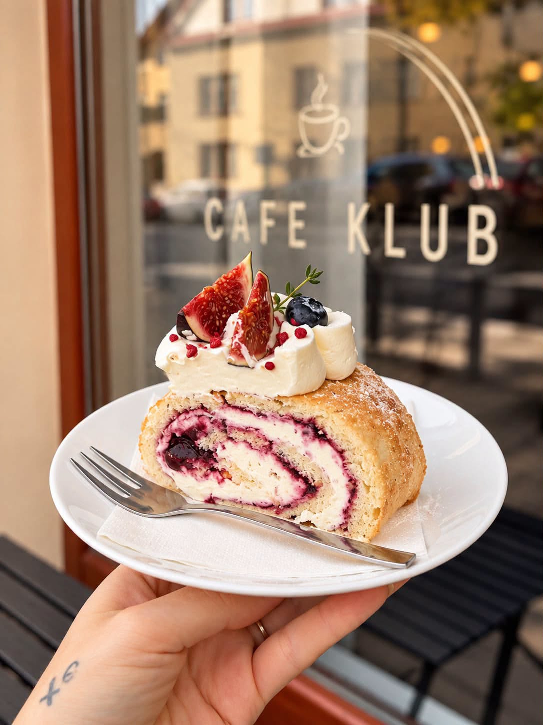 Kousek ovocné rolády na talířku před výlohou Kafe Klub